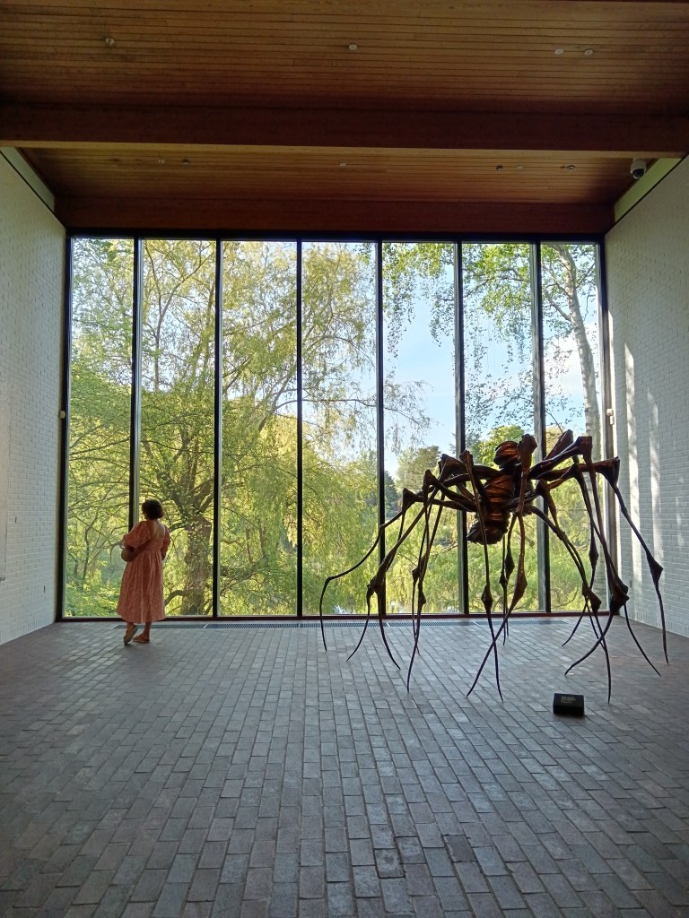 A spider sculpture in front of a window showing trees outside