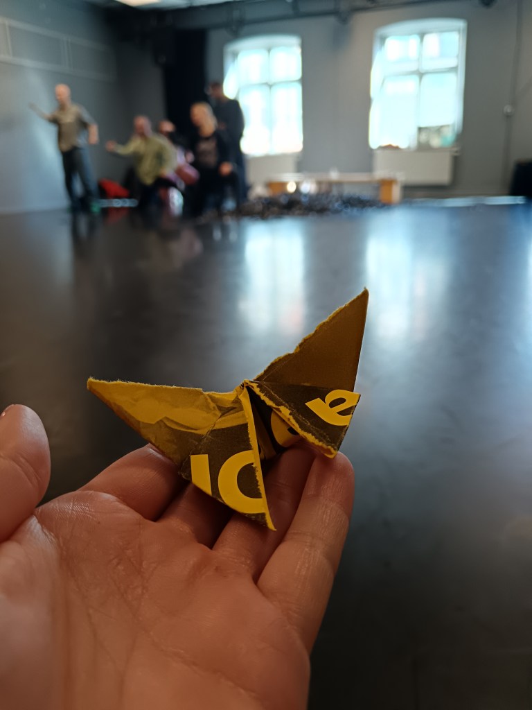 I hold a origami butterfly in front of rehearsing dancers