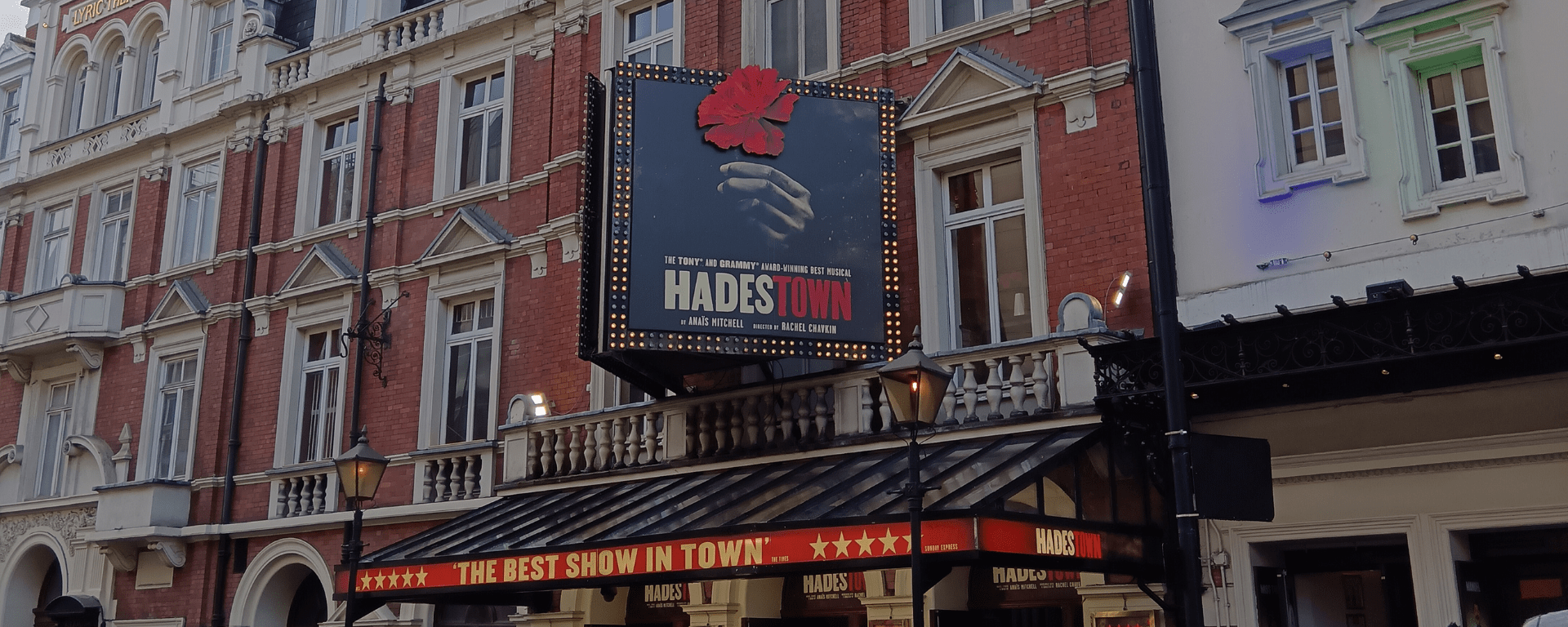 The exterior of a theatre in London with lights and signs that say Hadestown