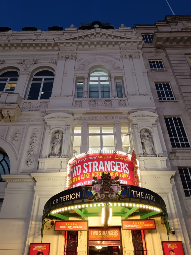 The front of the Criterion Theatre with signs for Two Strangers Carry a Cake Across New York