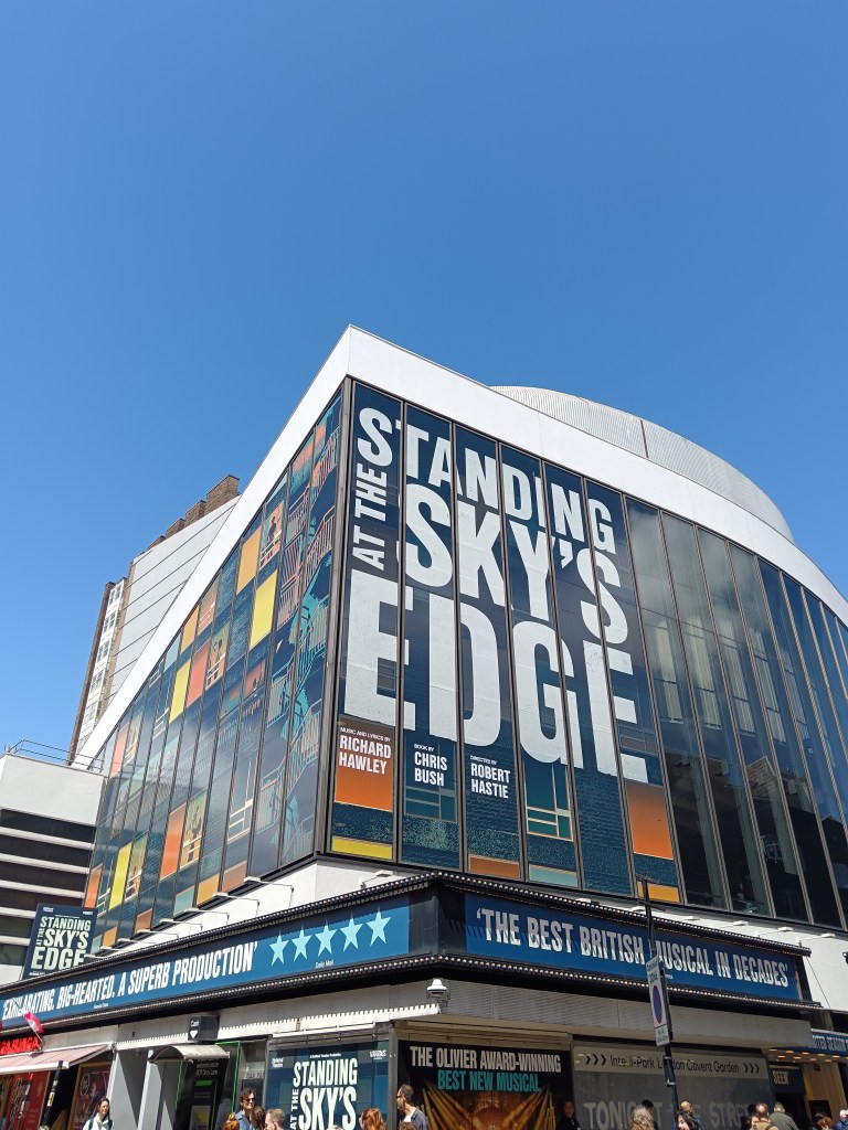 The Gillian Lynne theatre towers with a sign that says Standing at the Sky's Edge