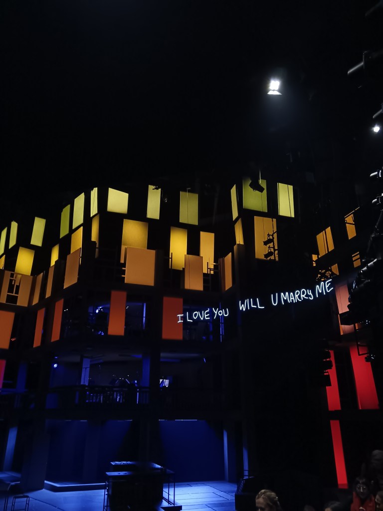 Yellow, orange and red squares hang alongside a neon sign that says I love you will u marry me