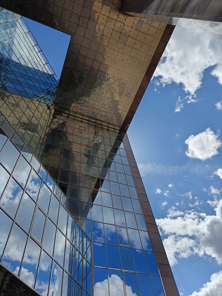 Sky and clouds reflect against a reflective angular building
