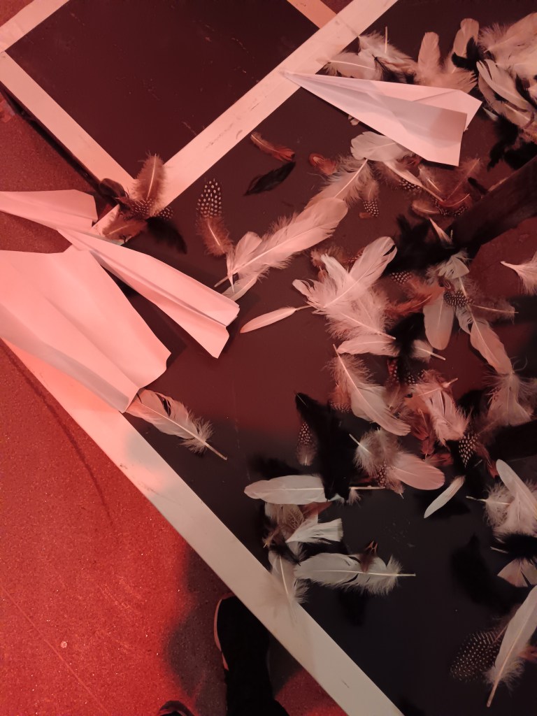 Paper airplanes and feathers on a stage floor