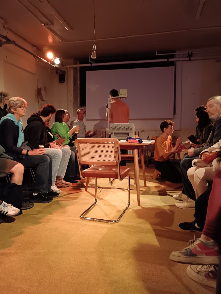 A small venue with a table and chairs between the audience