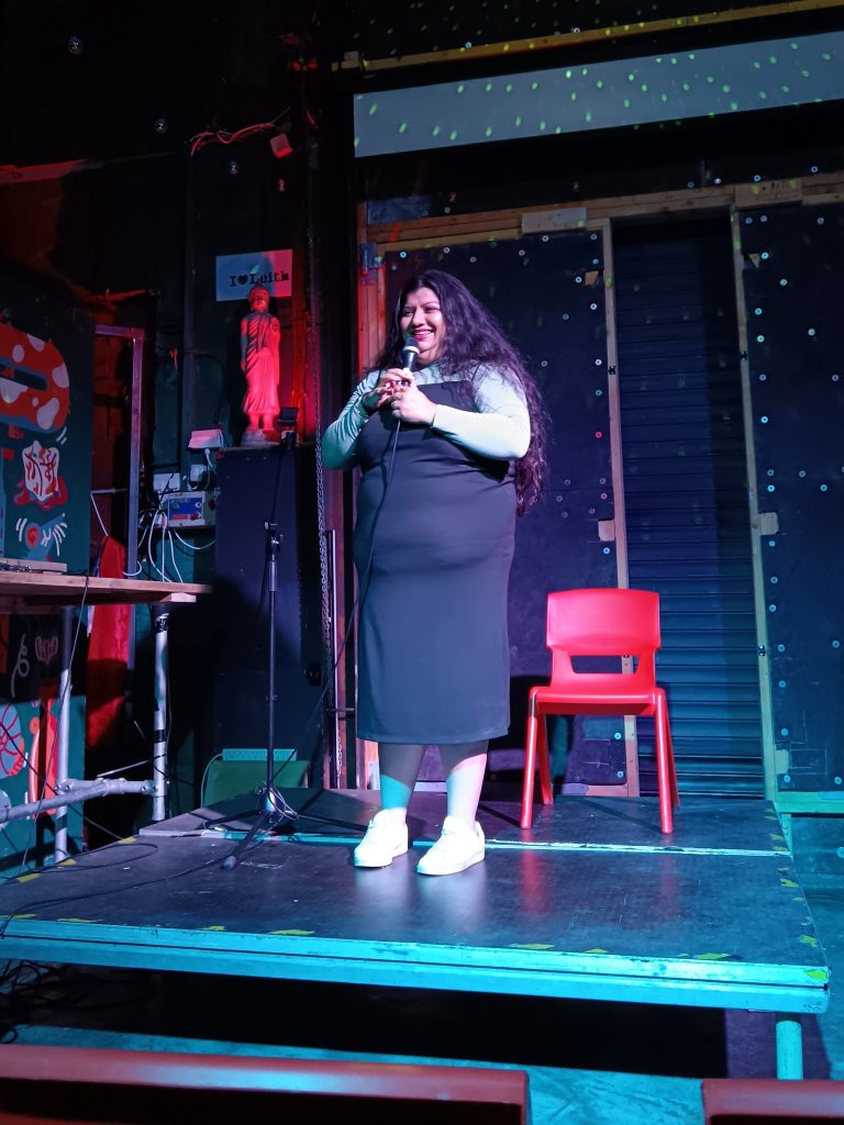 Sabina smiles on stage doing stand up