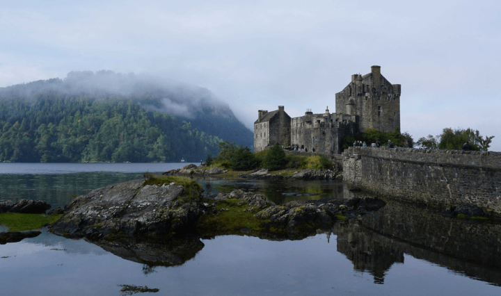 A castle framed by loch and misty tree covered mountains