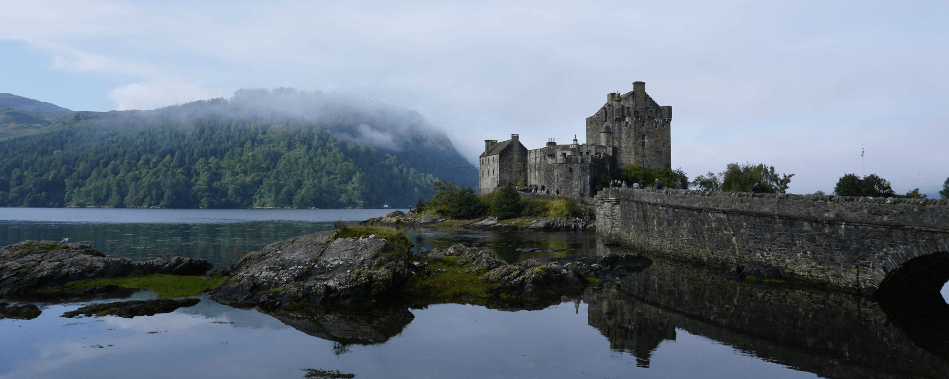 A castle framed by loch and misty tree covered mountains