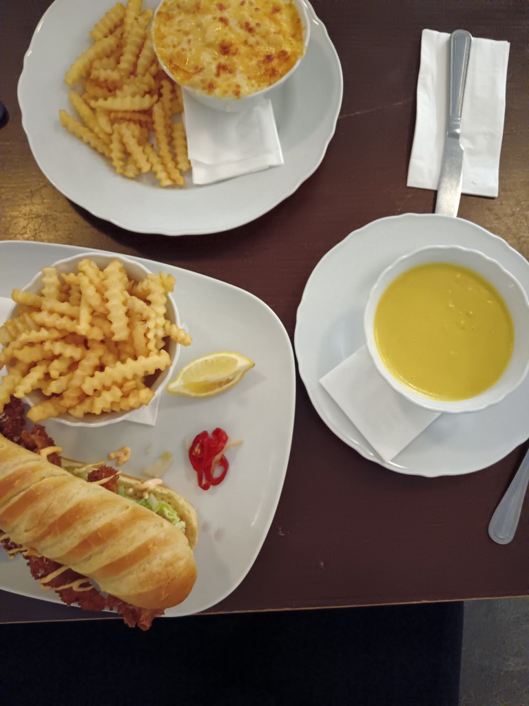 A haddock sandwich, corn chowder and mac n cheese on a table