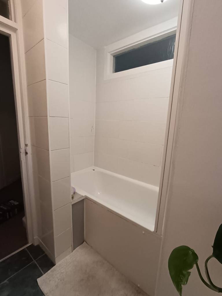 A white bath surrrounded by white tile