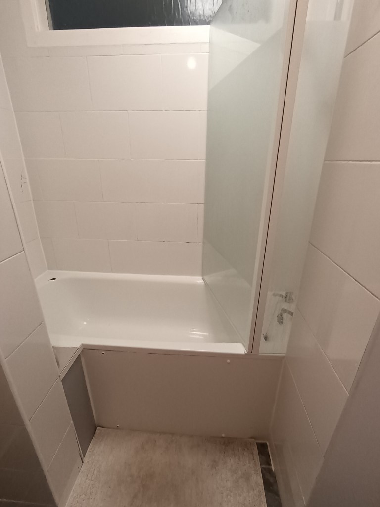 A white bath surrounded by white tile