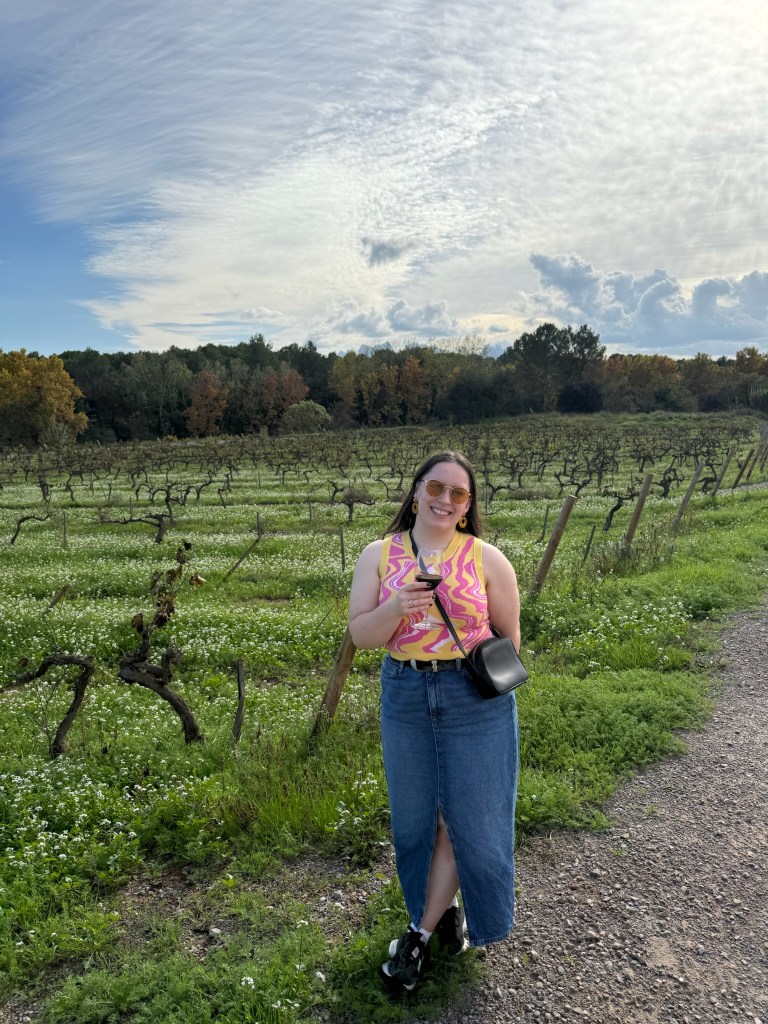 I smile in a vineyard holding a glass of wine