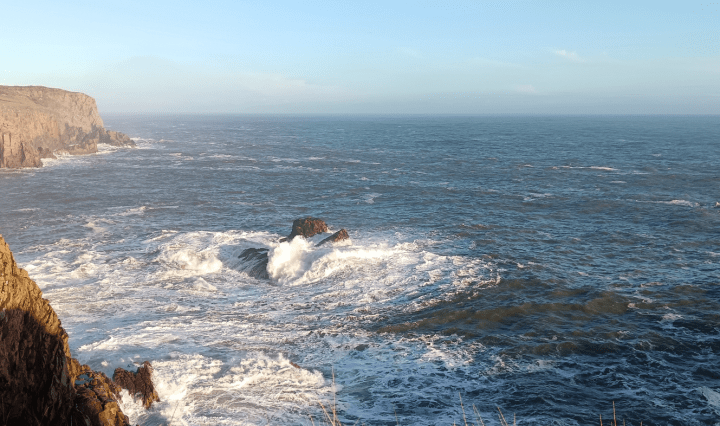 Waves crash around rocks under the cliffs