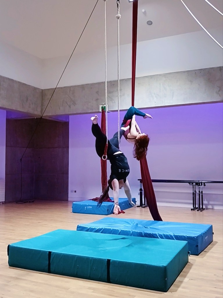 I hang down from a trapeze with my legs spread