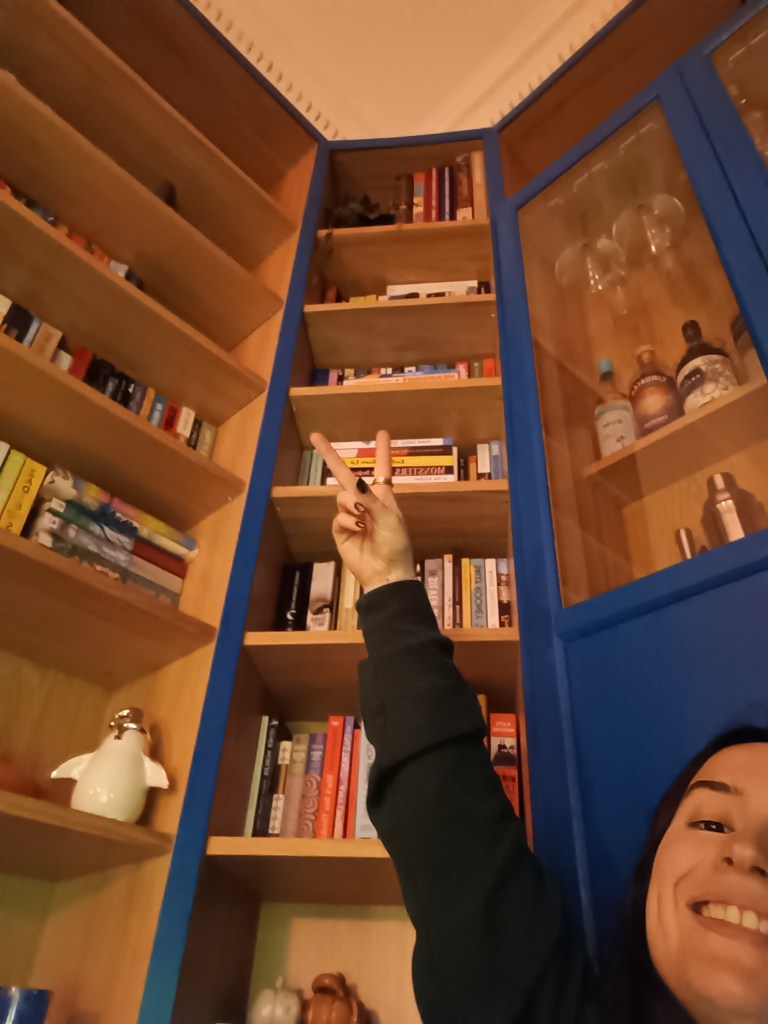 I throw a peace sign sitting with my bookshelves