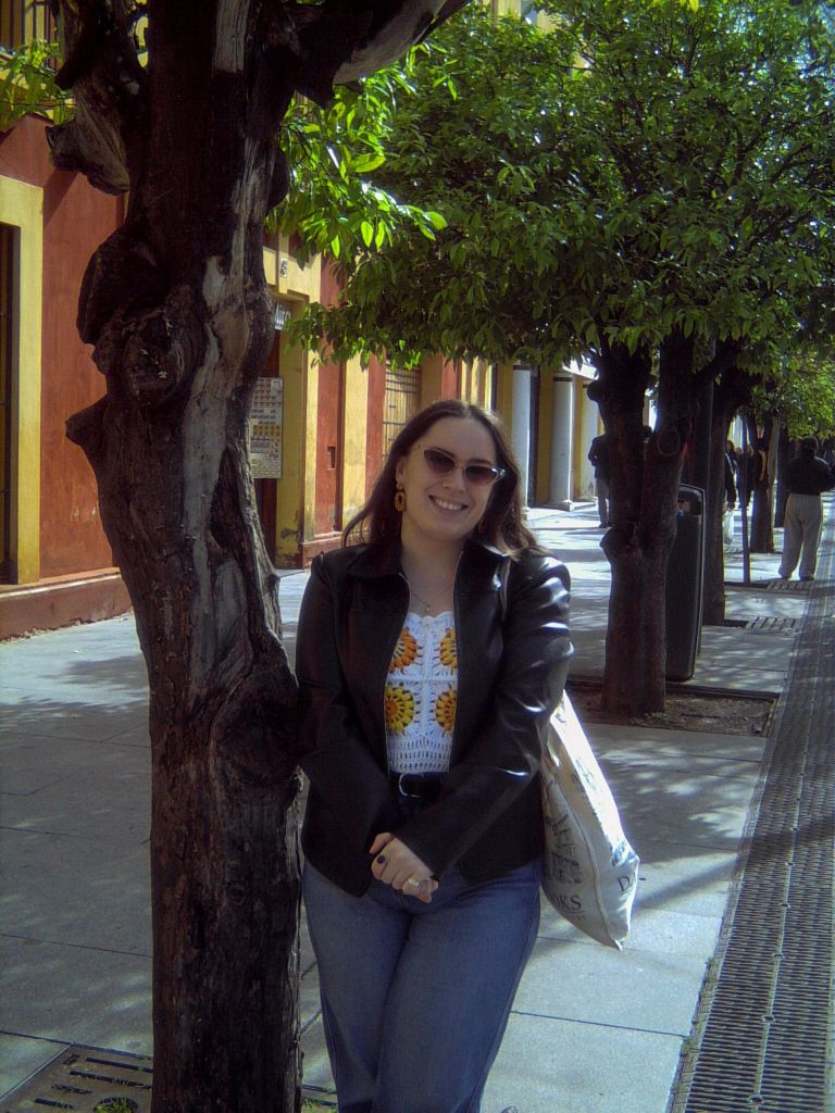 I smile standing by a tree on a colourful street