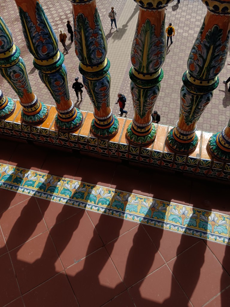 People in the gaps between hand painted spindles on a balcony