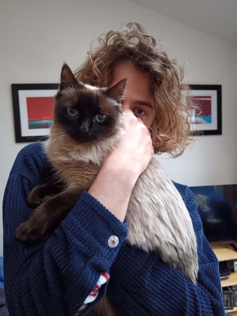 My curly haired boy holds a cat to his chest