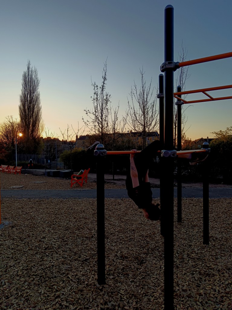 Ejay hangs upside down in the park at sunset