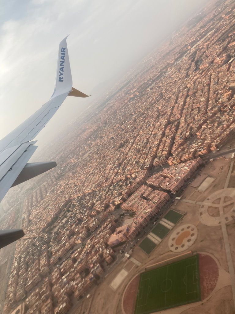 The plane wiing flying over rows of buildings
