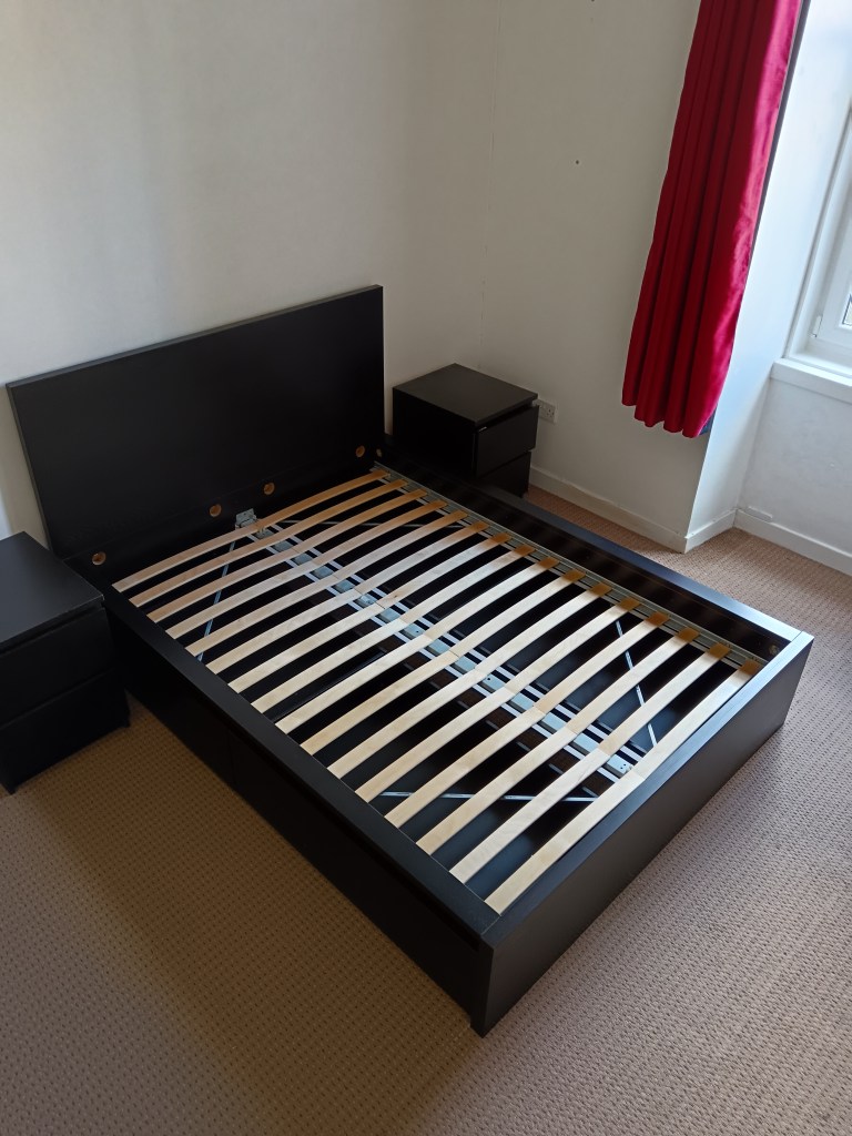 A big chunky black double bed with matching bedside tables