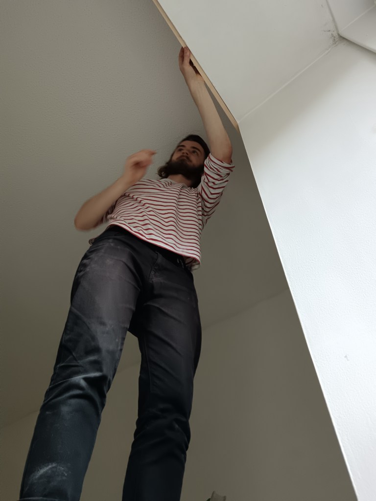 Kit stands on a ladder and measures the curtain rail holes on the wall