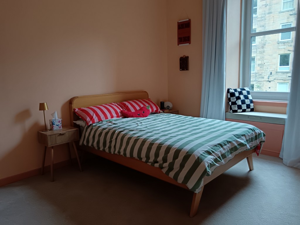 On the other side of the room is a rounded edge oak bed with colourful stripey bedding, wee bedside tables and the window seat