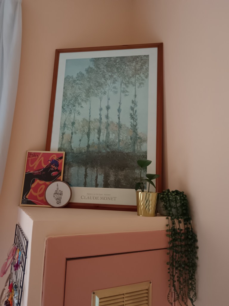 A large Monet print of trees in a large frame with a red illustration and an embroidery hoop in front and my pothos and string of pearls plants