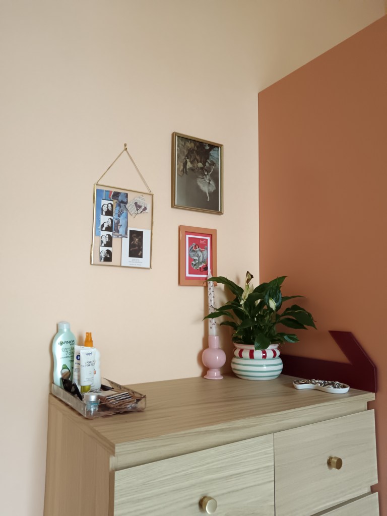 A trio of art pieces, one is a glass frame with a photo strip, post cards and pressed flowers, one is a Degas ballerina print and one is a postcard of an old vaudeville dancer. On the counter I have a peace lily in a colourfully striped pot and a painted candlestick