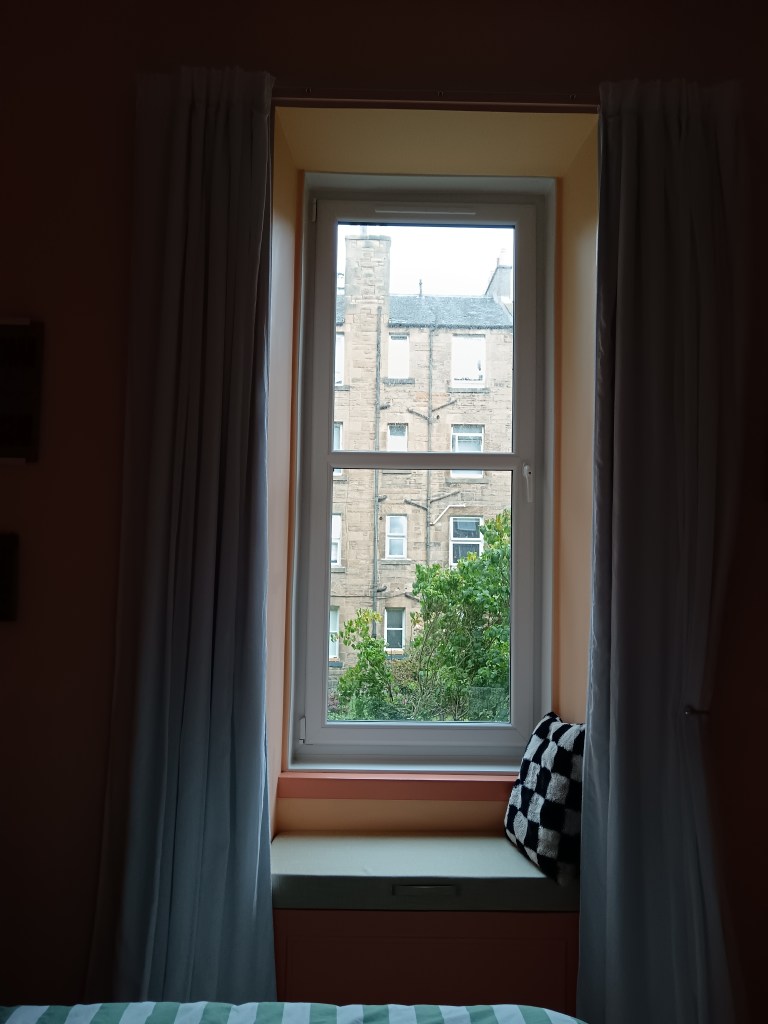 White curtains hang either side of the window and a checkered cushion sits on top of the window seat