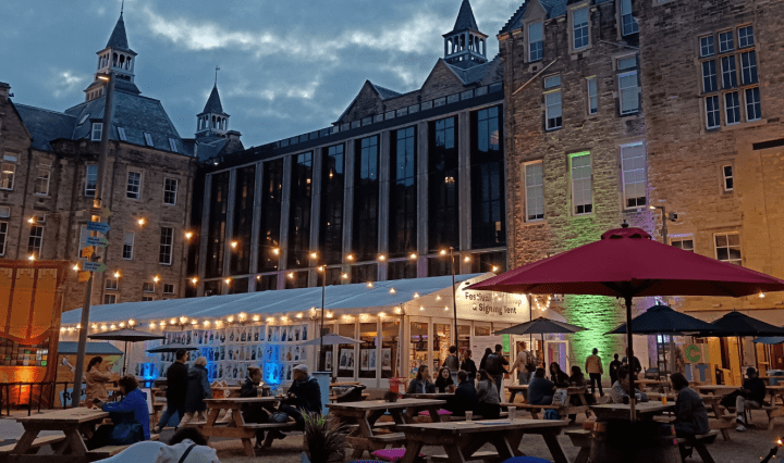 Outdoor festival site with strings of lights, tents and benches