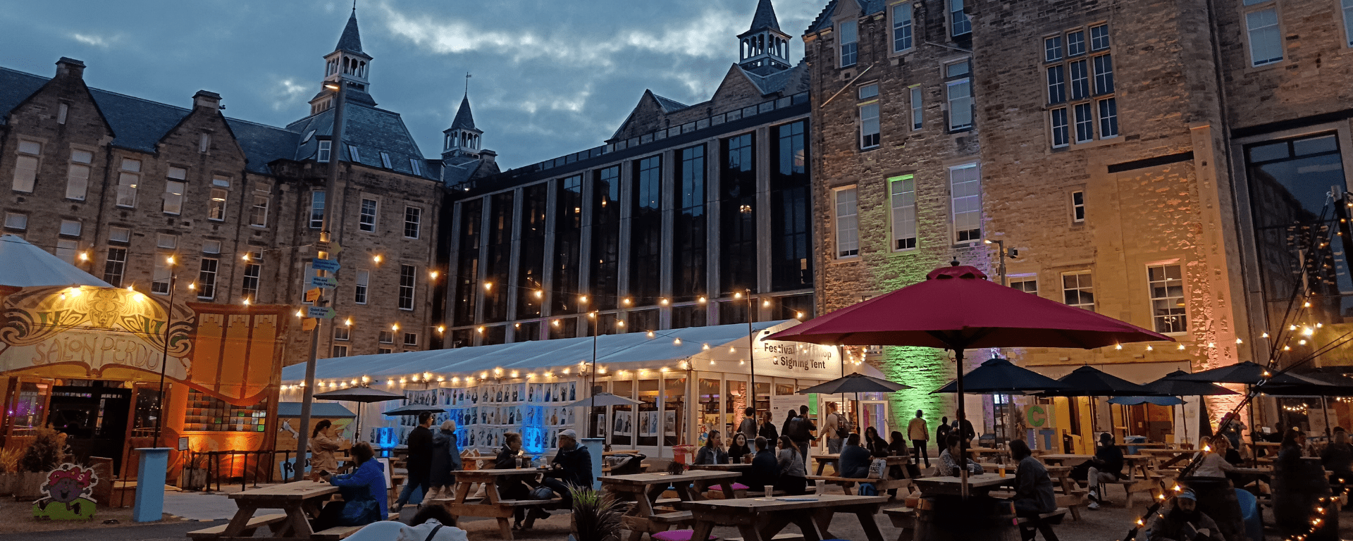 Outdoor festival site with strings of lights, tents and benches