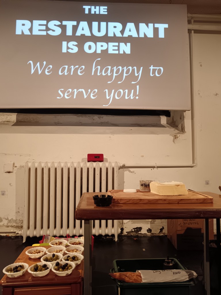 A screen says The restaurant is open we are happy to serve you and food sits on the table