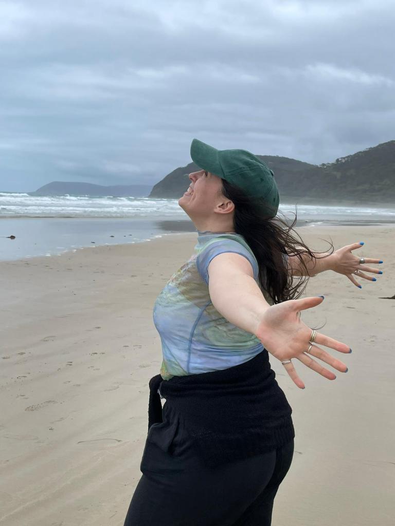 I smile and hold my arms out in joy on a beach