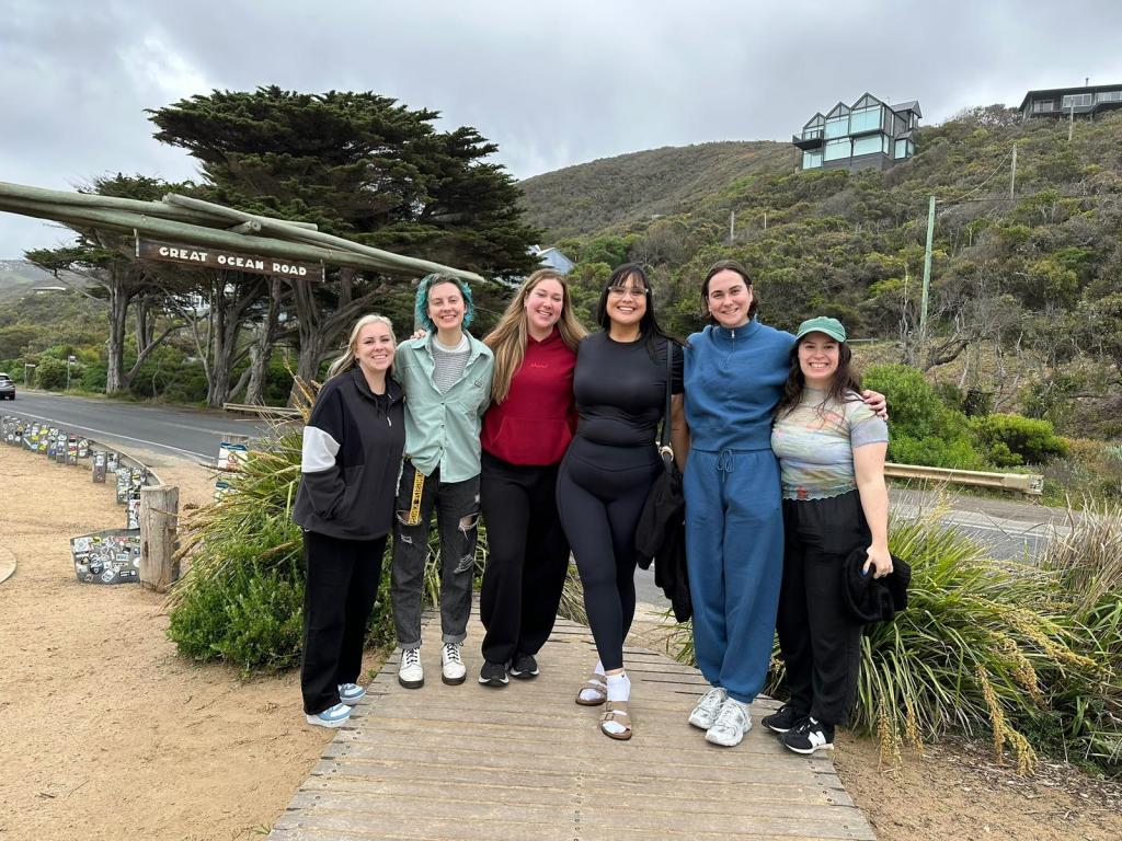 The group of tour gals smile together beside the Great Ocean Road sign