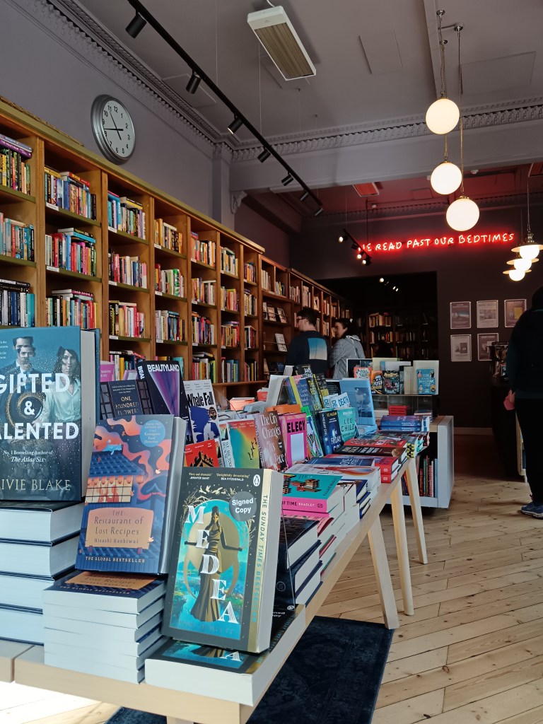 A gorgeous bookshop with a neon sign We Read Past our Bedtimes