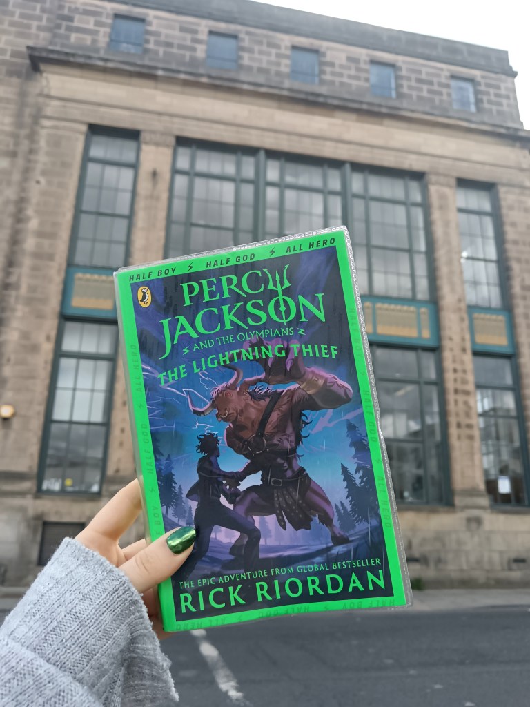 I hold The Lightning Thief in front of a Greek library