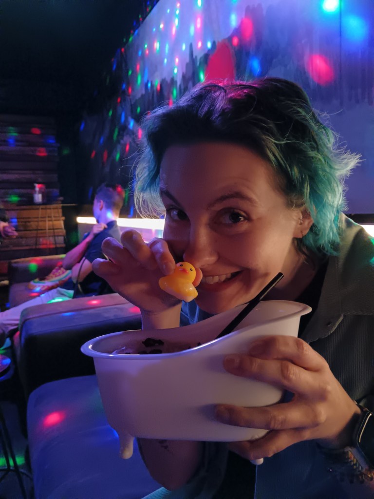 Ejay smiles with a tiny rubber duck as part of their bathtub cocktail