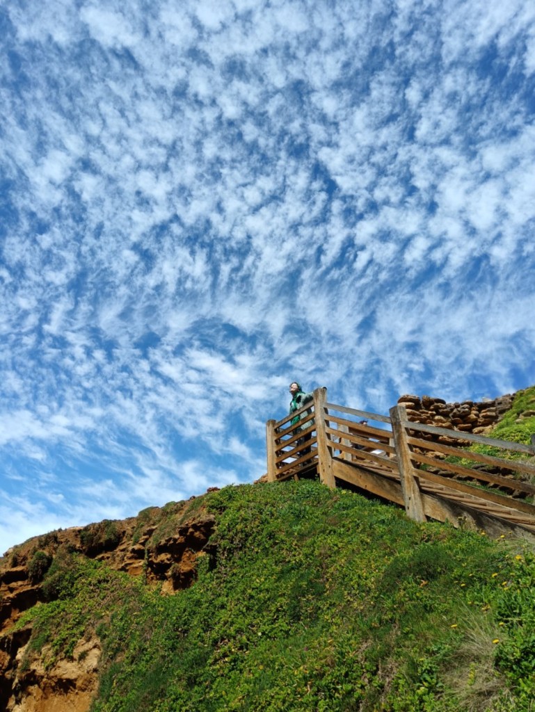 Ejay stands at the top of a staircase against a blue sky