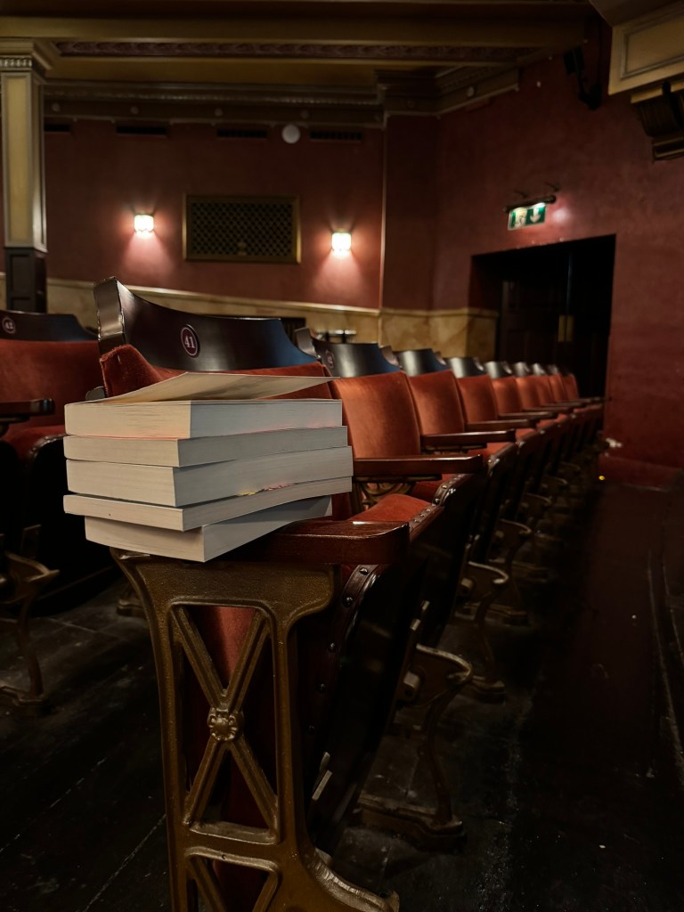 A stack of books sits on the end of a row of theatre seats