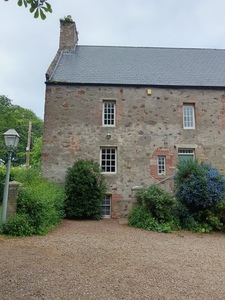 A big stone house framed with flowering bushes