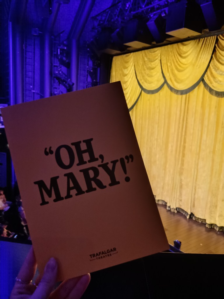 Holding an Oh Mary programme in front of the stage's yellow curtain