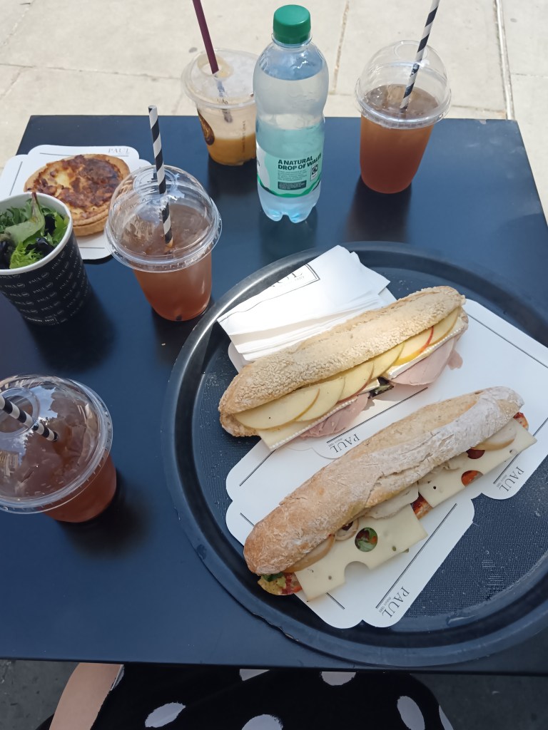 Some filled baguettes, a quiche and iced drinks on a cafe table