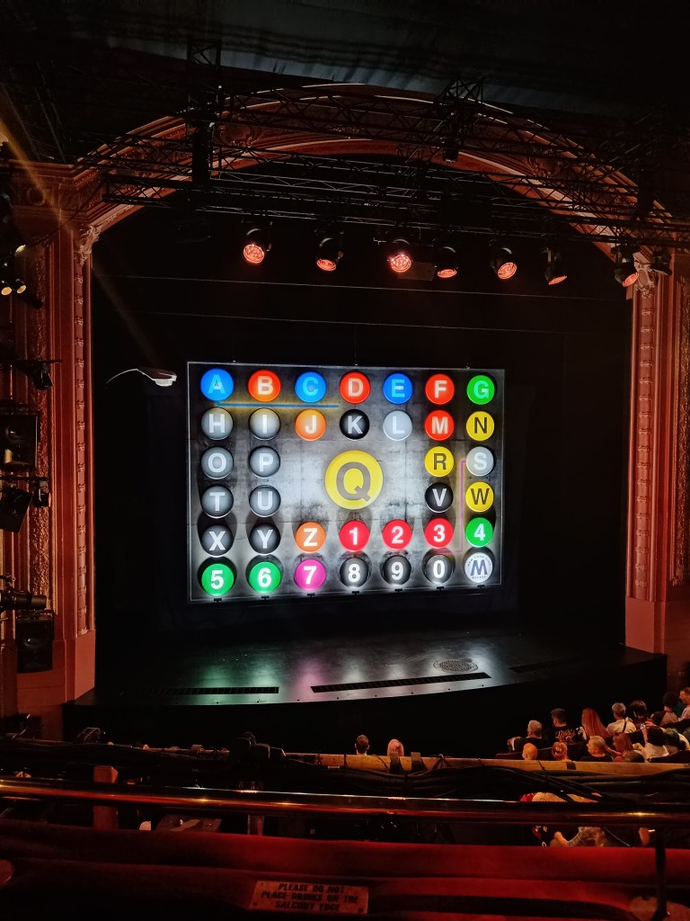 The Avenue Q stage has a screen showing New York subway numbers