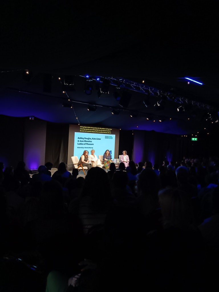 A panel of authors sit on stage in front of a full crowd