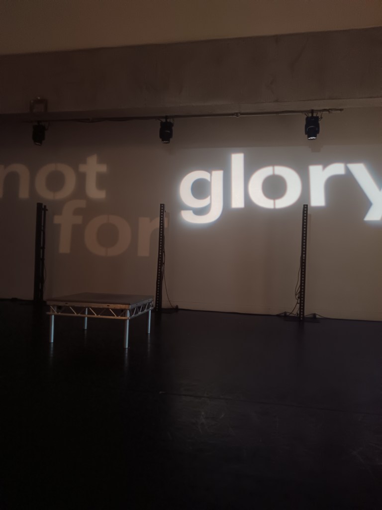 words not for glory are projected on a wall behind a wee elevated stage