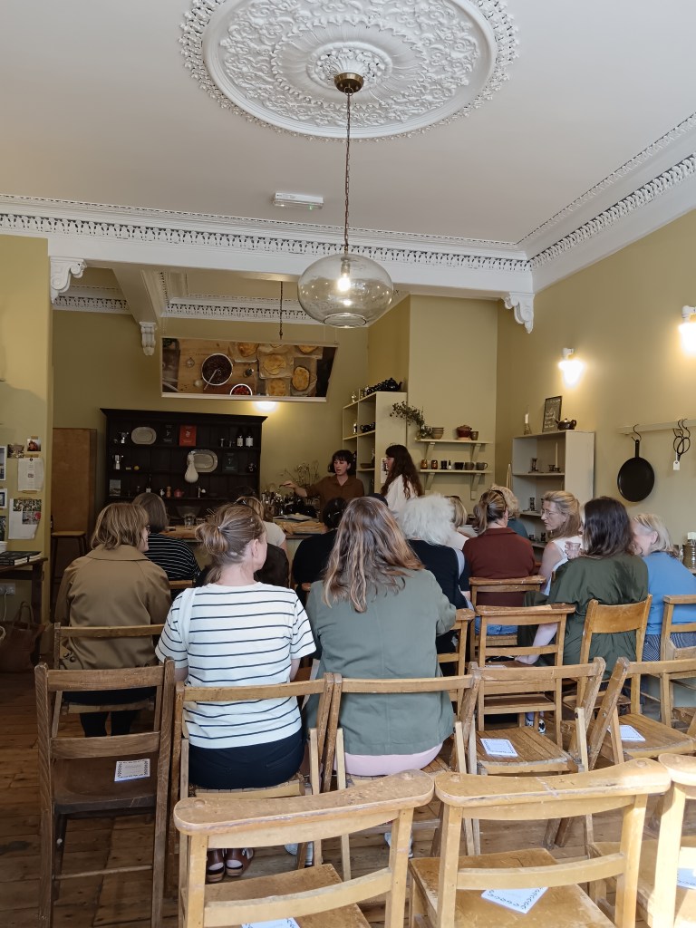 A room full of people watching a kitchen counter with a mirror mounted above it
