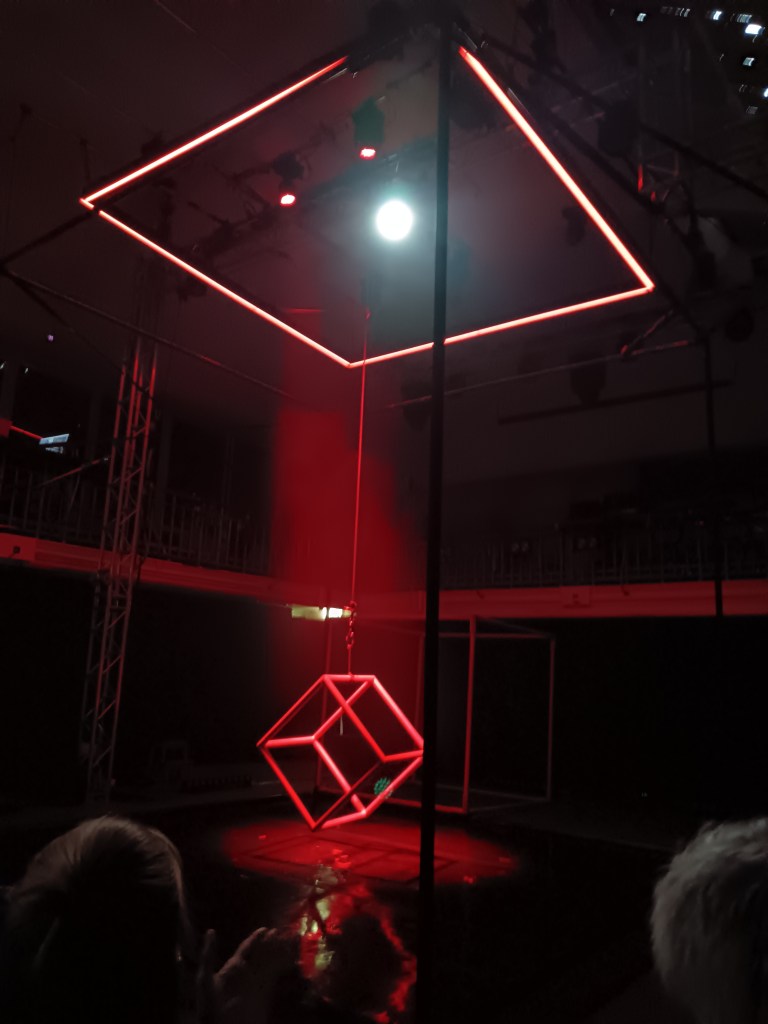 A red cube hangs from a string inside a square frame of light