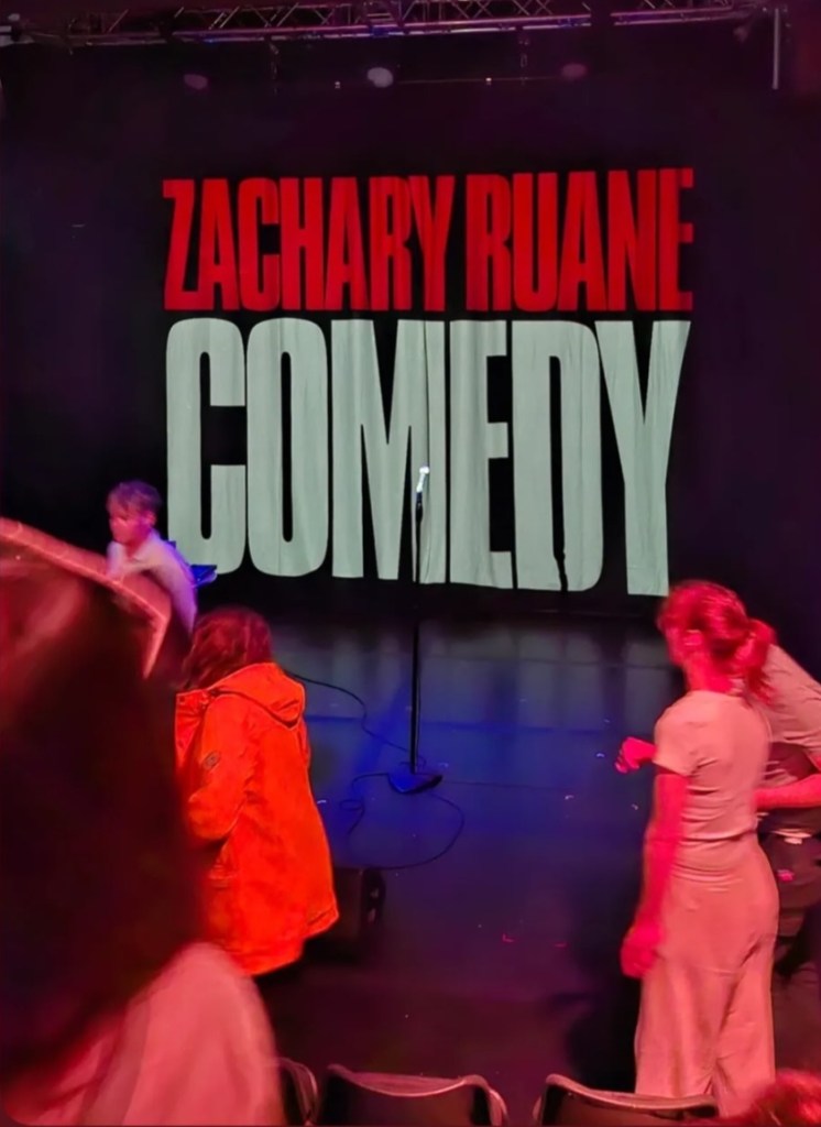 Zachary Ruane Comedy is projected on a curtain